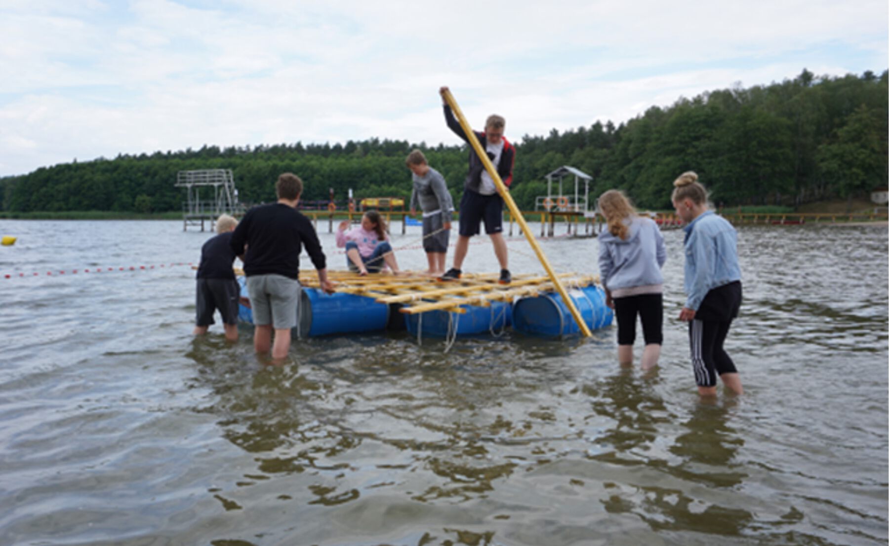 Jugendliche auf und neben einem Floß im Wasser
