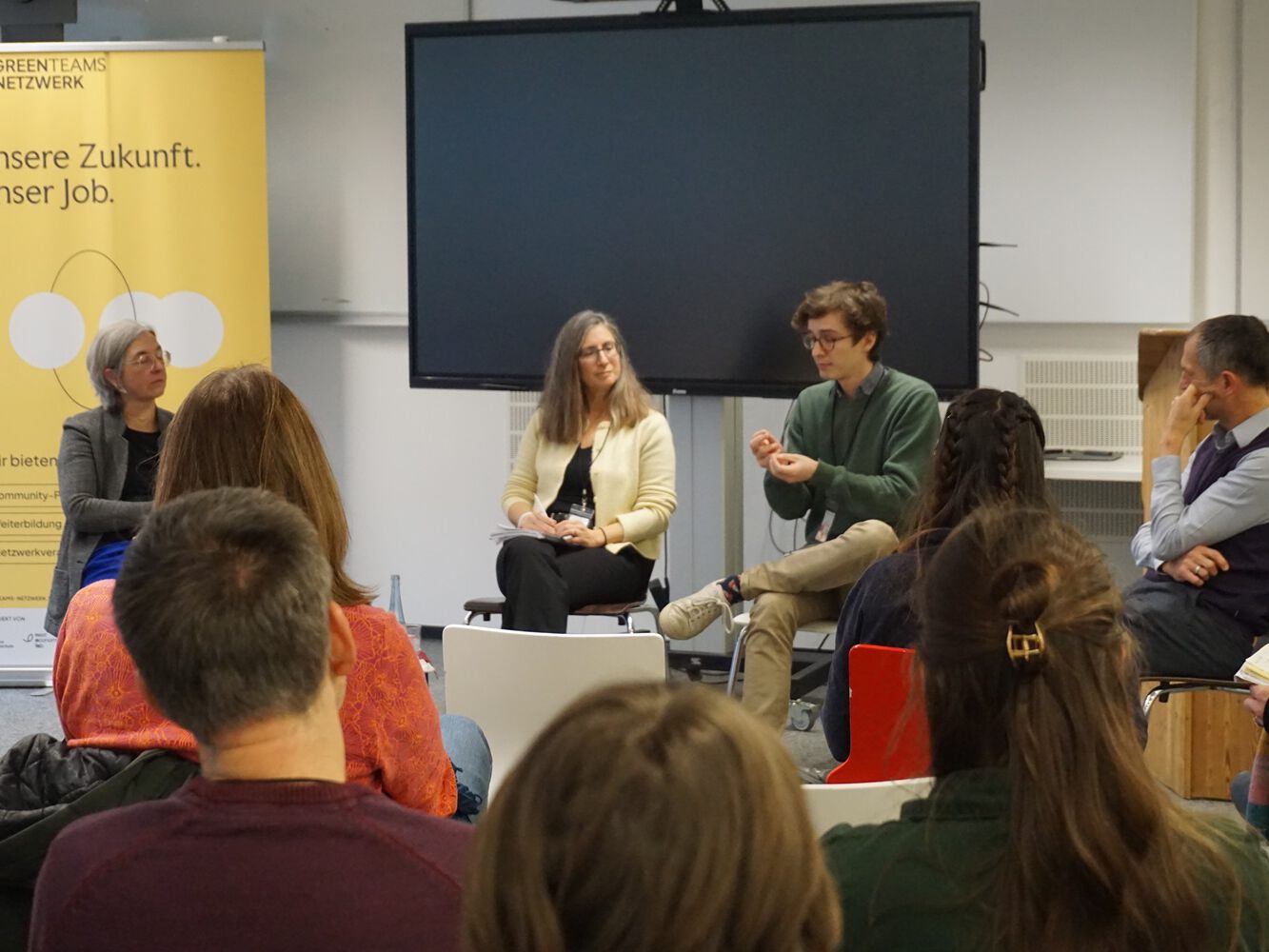 Mehrere Personen sitzen in einem Workshop, eine Frau moderiert.
