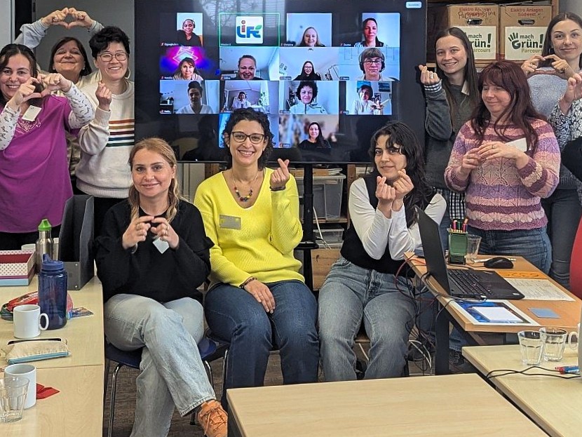 Mehrere Frauen sitzen vor einem Bildschirm mit Kacheln von einer Onlinekonferenz